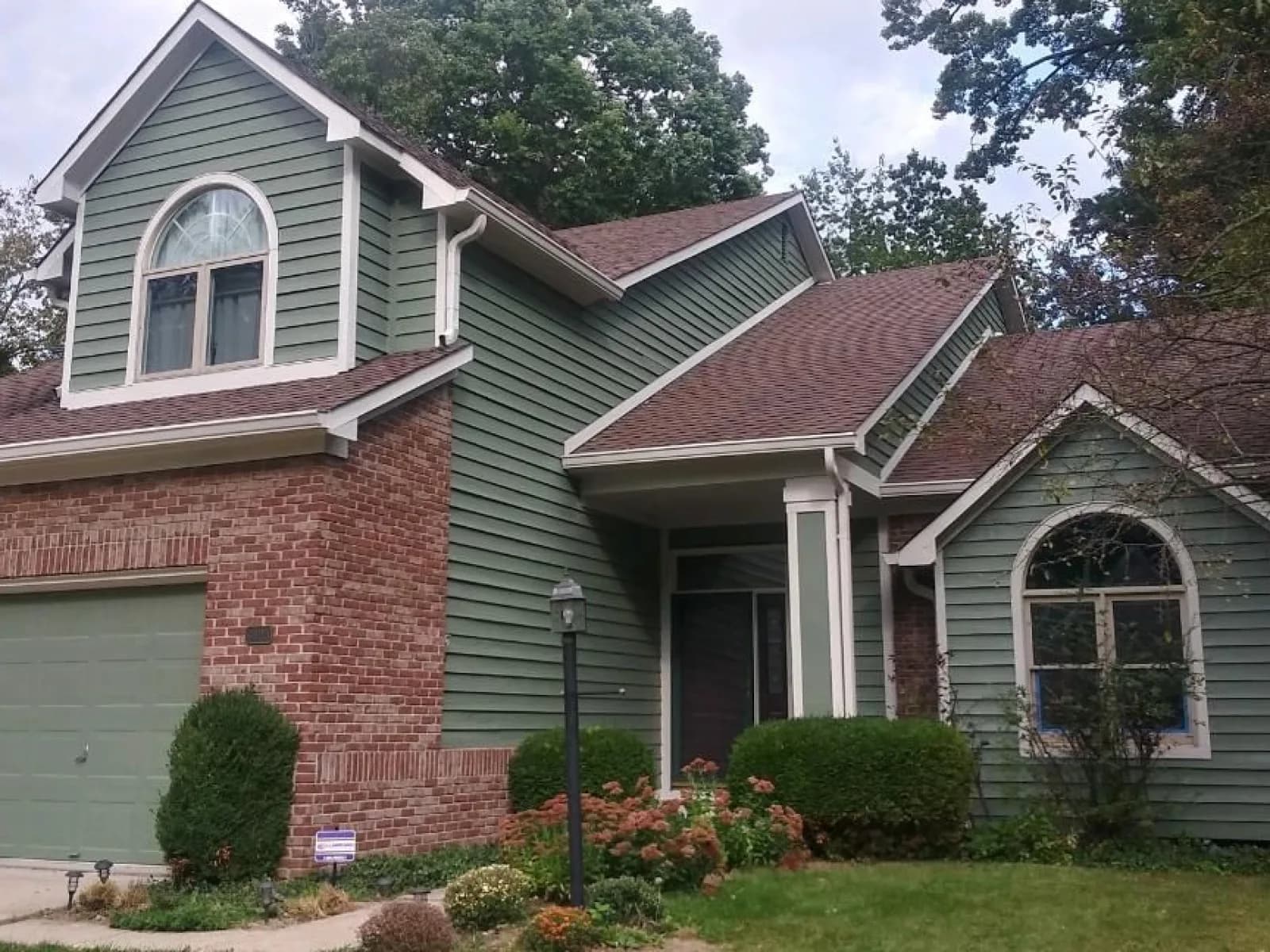 Siding repainted green on a two-story, brick untouched